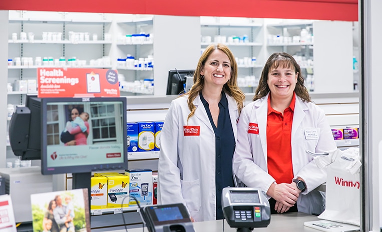 Two pharmacists standing behind the pharmacy counter and smiling